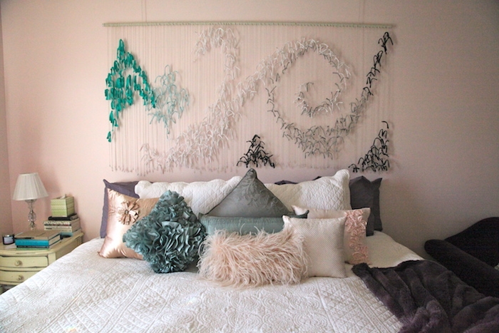 deco tete de lit en plumes vertes, blanches, noires, sur des fils blancs, coussins en vert, gris et rose, linge de lit blanc