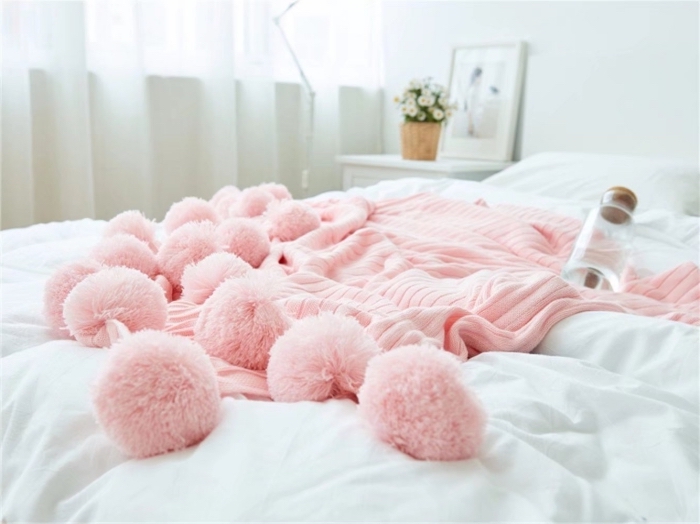 ambiance cocooning dans la chambre à coucher blanche avec modèle de plaid de couleur rose pastel décoré de grands pompons