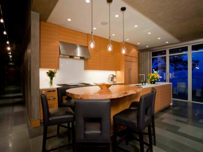 cuisine avec ilot central, table en bois naturel, ilot rectangulaire, chaises noires, lampes suspendues
