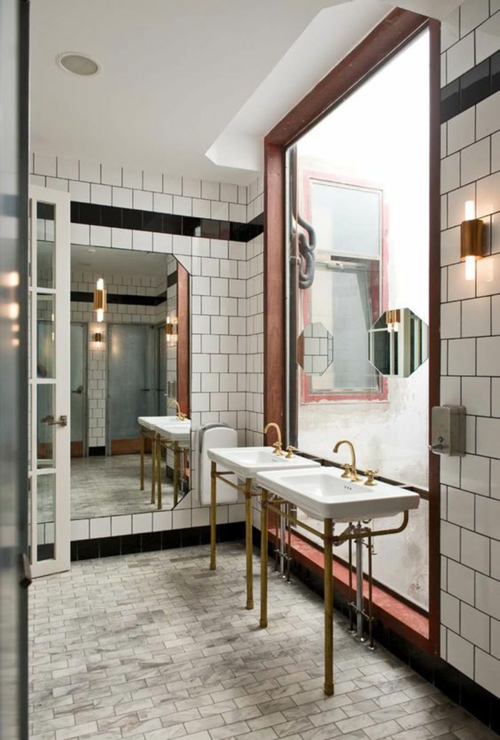 salle de bains avec des murs recouverts de carrelages blancs, carrelages du sol en gris, grand miroir carré bien illuminé, deux lavabos vintage avec des tubes et des éviers en couleur or, habiller un mur en carrelages 