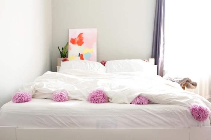 linge de lit blanc décoré de pompons et tete de lit originale en tableau décoratif art abstrait derrière le lit