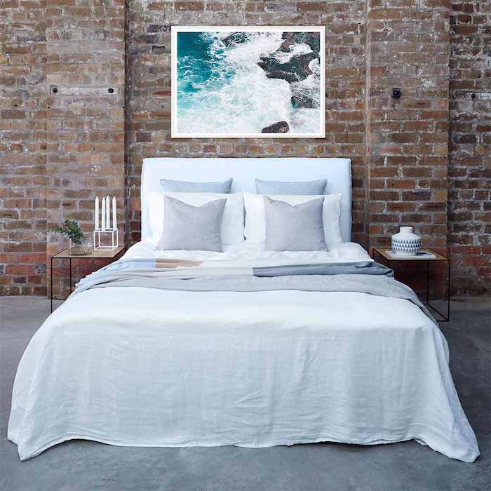 modèle de tete de lit en cadre photo paysage bord de mer avec linge de lit blanc et gris, mur en briques derrière le lit, deco style industrielle