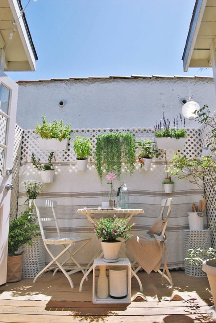idee deco terrasse en style bohème, balcon fleuri, decoration jardin terrasse, meubles de jardin vintage en métal blanc, sol recouvert de bois clair, mur végétal porte-plante avec des pots blancs 