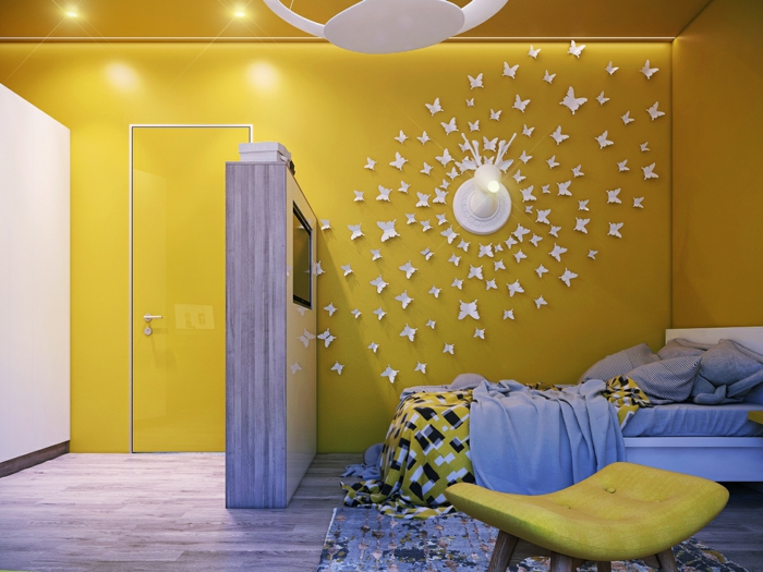 une chambre d'enfant aux murs et plafond peints en jaune brillant, sol recouvert de parquet gris, applications de papillons en carton blanc qui tournent autour d'une applique murale, déco murale, luminaire blanc au plafond en forme de disque