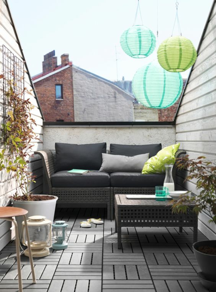 idee amenagement terrasse avec des meubles en rotin et des coussins noirs, table rectangulaire basse avec des ornements orientaux, lame bois au sol, lanternes en carton en vert réséda et bleu pastel suspendus au plafond 