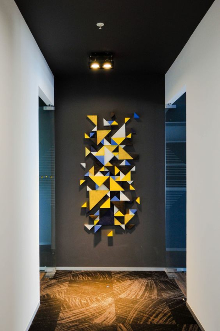 une idée pour un pan de mur aux motifs graphiques en formes de triangles en jaune et bleu roi, sol effet usé, murs blancs, plafond noir