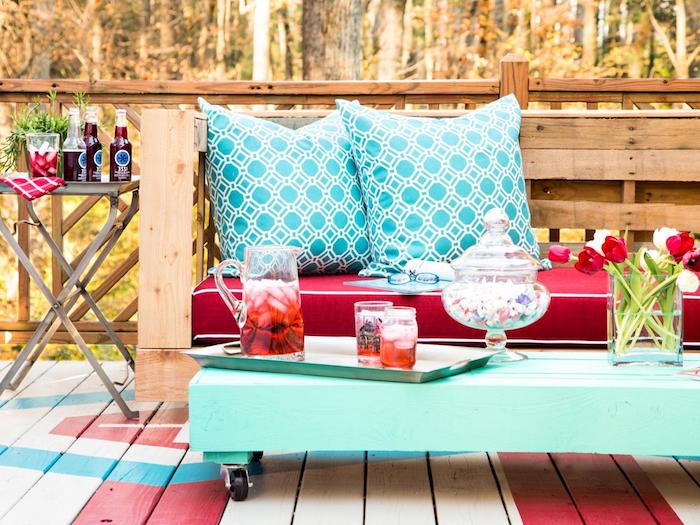 exemple de salon de jardin en palette avec un canapé bois avec coussin d assise rouge, coussins décoratifs bleus et une table basse en palette repeinte en bleu à roulettes, deco terrasse