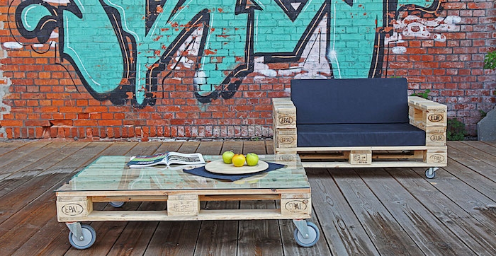 meuble avec palette en bois, table basse palette à roulettes et canapé en bois avec coussin d assise noire, mur en graffiti