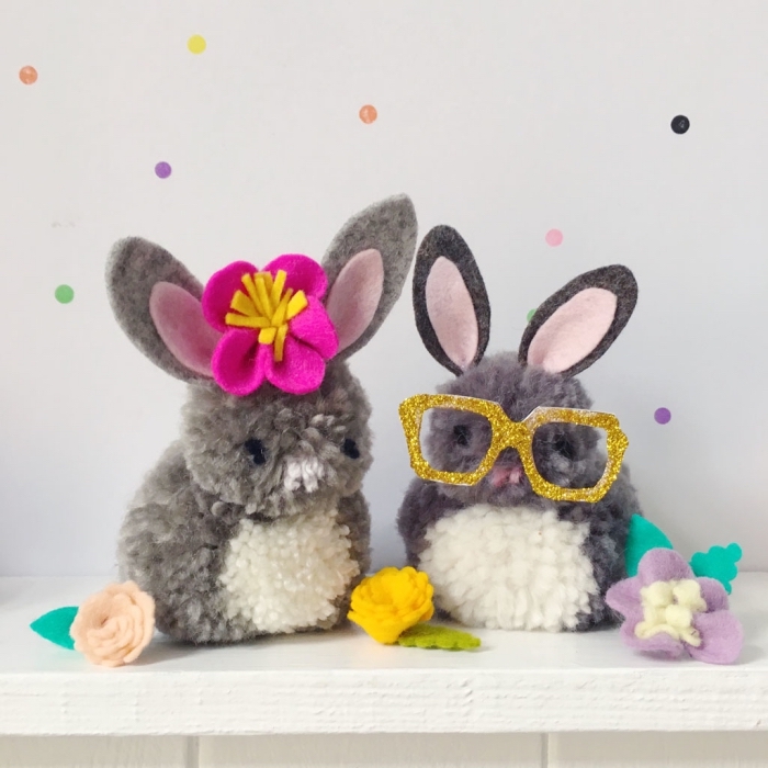 couple de lapins doudou fabriqués en pompons de laine et décorés avec accessoires chic en forme de lunettes et couronne florale pour la tete