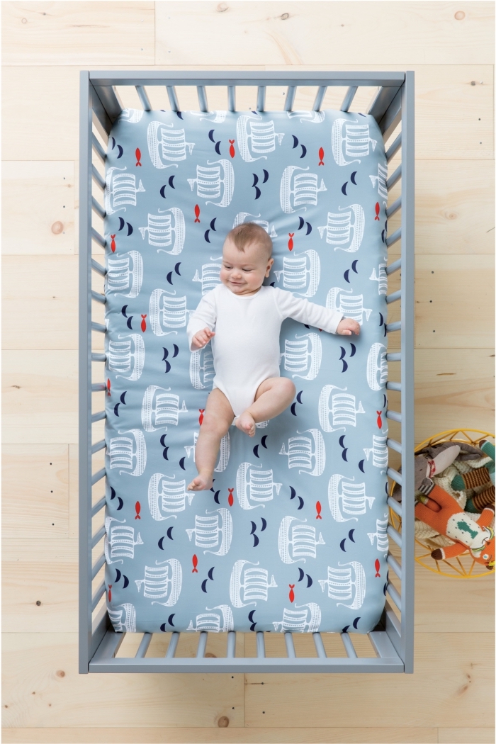 couverture de lit bleu clair avec bateaux blancs pour un linge de lit dans la chambre nouveau-né au plancher de bois clair et lit bébé gris clair