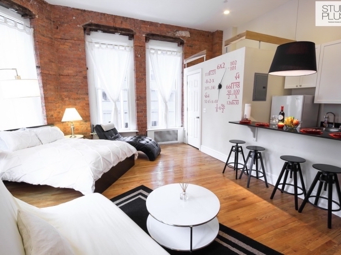 style loft industriel dans un aménagement studio avec cuisine ouverte en blanc et gris, meubles blanc et noir sur plancher de bois marron