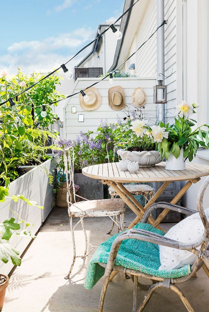 idee amenagement terrasse en style bohème, balcon fleuri, decoration jardin terrasse, meubles vintage, trois chapeau de paille accrochés au mur blanc 
