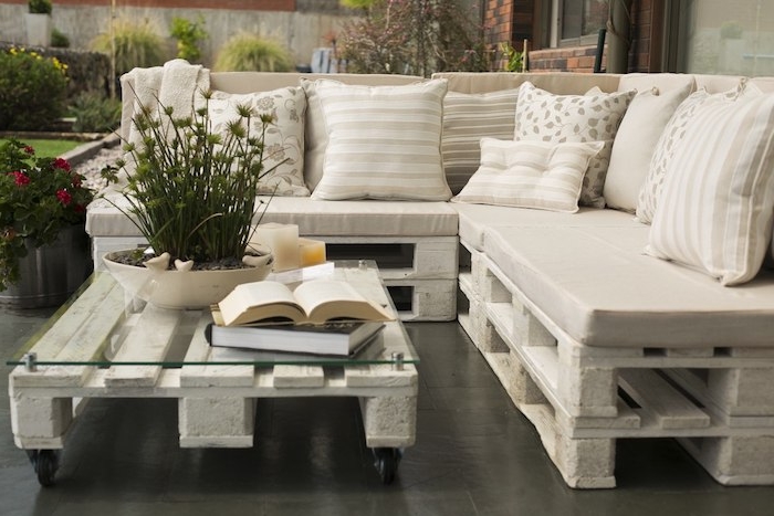 modèle de canapé en palette blanchi avec coussins beige, gris et blanc, table basse en palette avec plateau en verre à roulettes