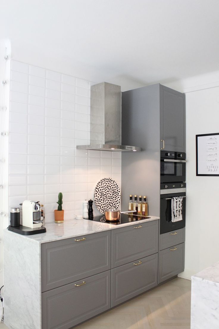 cuisine grise et blanche au design élégant associant des meubles à façades grises avec des poignées dorées et un comptoir en marbre