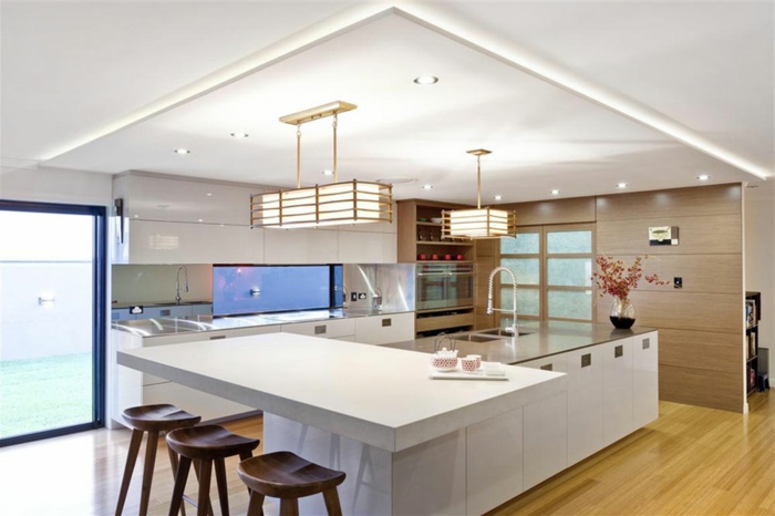cuisine avec ilot élégante, îlot de cuisine blanc, chaises en bois, faux plafond lumineux, sol stratifié
