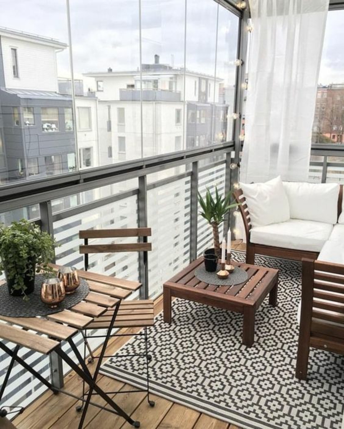 aménagement terrasse appartement, idée déco terrasse, tapis motifs graphiques en noir et blanc, table et chaises IKEA pliables, canapé de jardin massif d'angle, voilages blancs