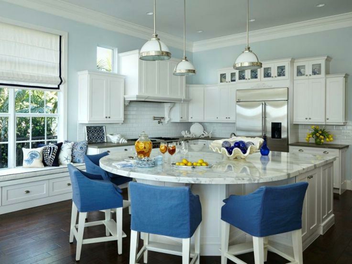 modele de cuisine avec ilot central, chaises bleues, ilot et table en forme courbée, murs bleus, grande fenêtre et banquette