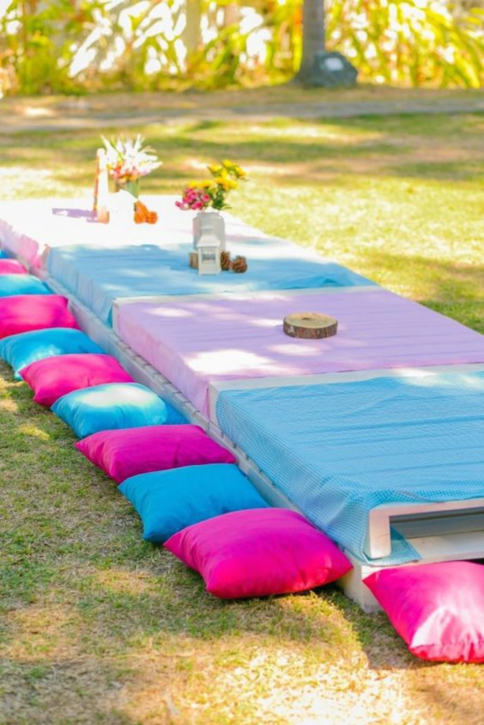 amenagement exterieur, deco jardin pas cher, tables basses en palettes avec des nappes en couleurs pastels, coussins pour s'asseoir en fuchsia et bleu pastel