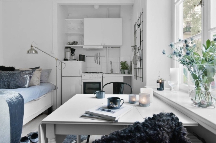 ambiance cozy dans un studio étudiant avec grande fenêtre aménagé avec petite cuisine blanche et grand lit 