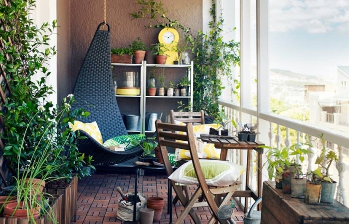 oasis sur le balcon avec mobilier de jardin en bois foncé et une chaise suspendue noire couverte de coussins à motifs tropicaux