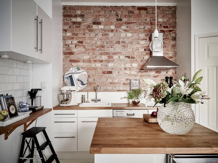 déco de style industriel avec pan de mur en briques rouges dans une cuisine aux armoires blanches avec comptoirs de bois massif