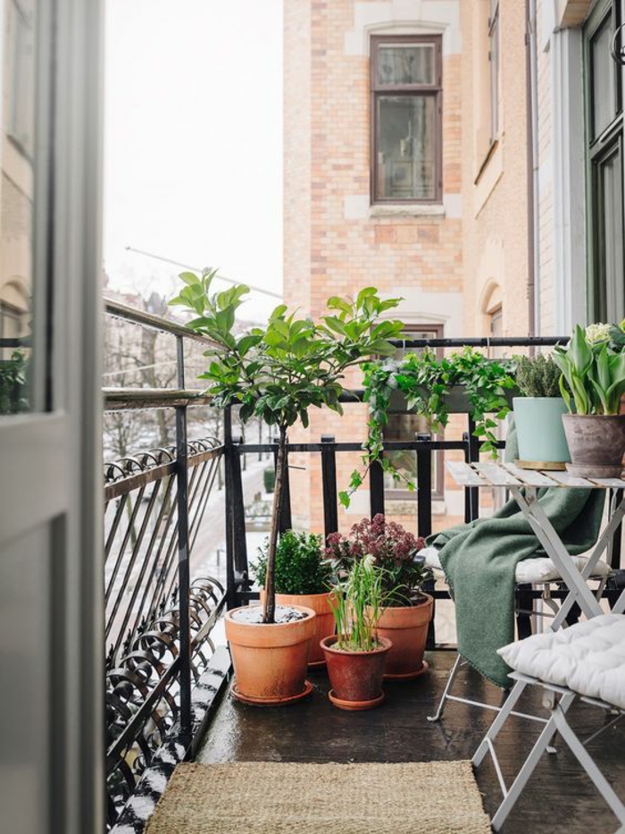 petite terrasse parisienne, idee amenagement terrasse, six pots avec des plantes vertes, sol recouvert de dalles en noir lisses, tapis en paille, chaises et table pliable en métal gris