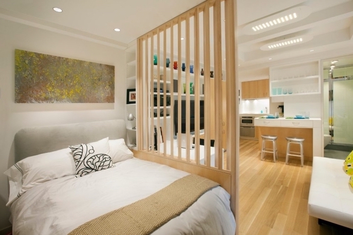 chambre à coucher avec grand lit et séparation de bois dans un studio aménagé en blanc et noir avec petite cuisine