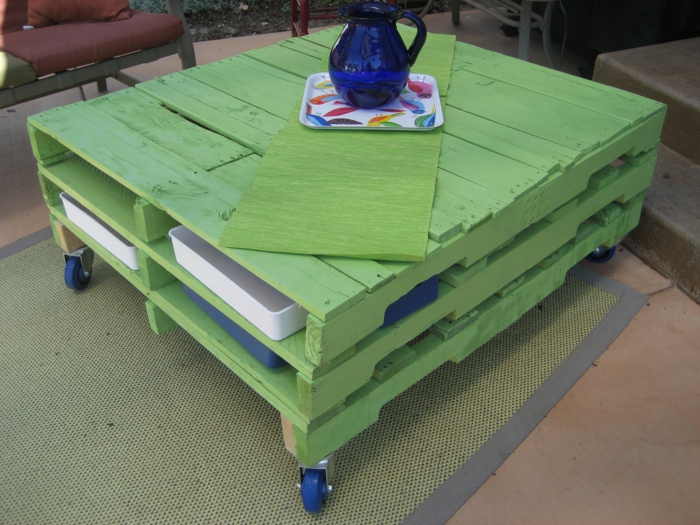 salon de jardin palette, meubles de jardin en palettes, table basse carrée en taille grande, avec bois peint en vert réséda, des roues bleues pour la rendre mobile