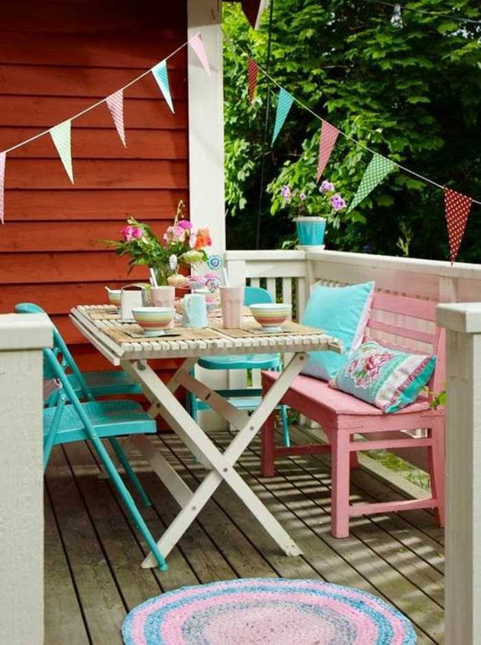 deux chaises pliables en métal bleu pastel. un banc en bois rose avec deux coussins en turquoise et rose, déco jardin récup, table pliable en bois blanc avec couverture jaune, petit tapis rond en rose et bleu pastel