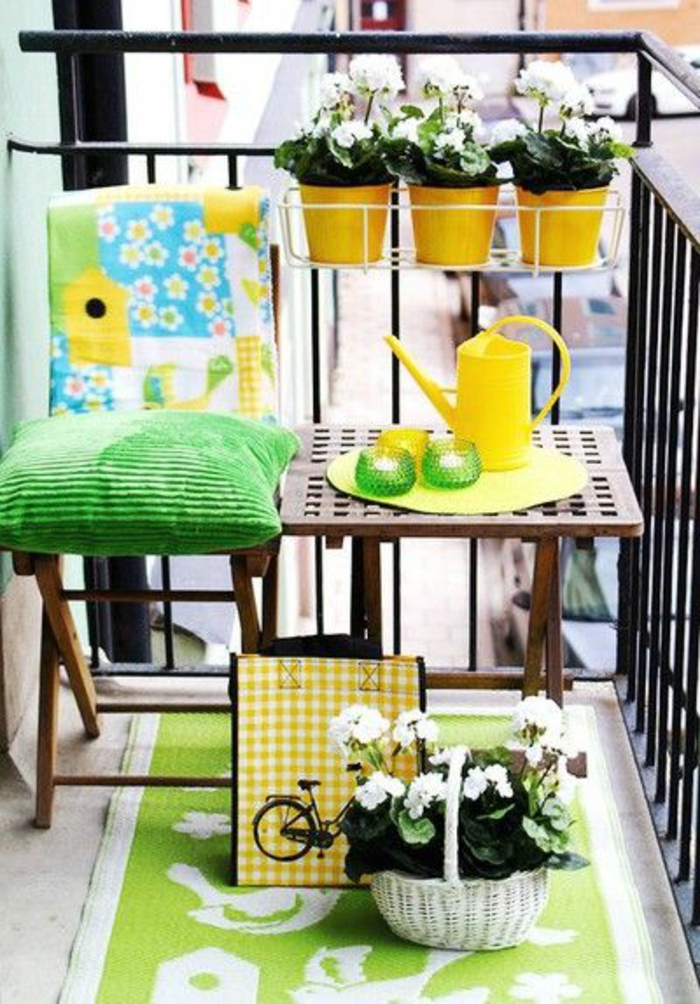 espace aménagé en couleurs vibrantes, idée déco terrasse en vert et jaune, trois pots jaunes sur le garde-corps, tapis en vert réséda et blanc avec des motifs oiseaux, coussin vert pomme sur une chaise pliante en bois marron