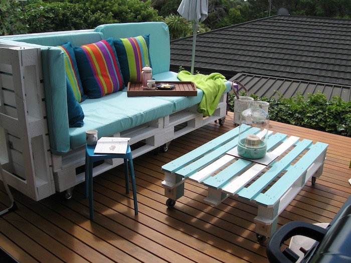 coussin salon de jardin palette bleu sur un canape palette blanchi, table basse avec palette à roulettes, terrasse bois