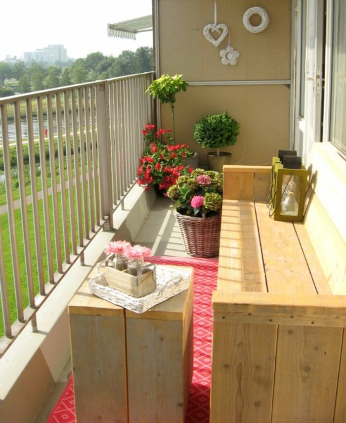idee amenagement terrasse, balcon fleuri, banc long en poutres de bois avec une lanterne posée au bout, table en poutres de bois en forme carrée, tapis rouge et blanc, pots avec des fleurs rouges 