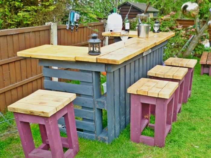 bar extérieur pour le jardin avec plan en bois clair, tabourets avec la base en bois de palettes peint en couleur fuchsia, base du bar en couleur gris pastel
