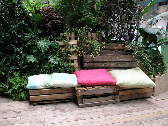 mur végétal extérieur avec une banquette en planches de bois de palette, coussins vert, rose et bleu, terrasse bois