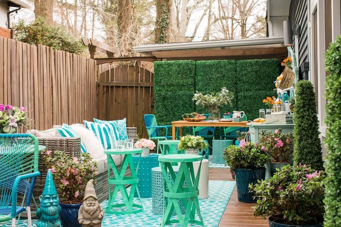 amenagement terrasse exterieure, un salon de jardin composé d un canapé cocooning, plusieurs tables basses rondes, nains de jardin, cloture bois, mur végétal extérieur, tapis bleu, coin repas à côté