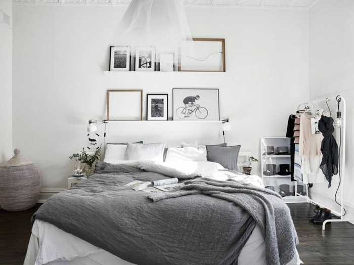chambre à coucher adulte moderne style scandinave, sol en bois foncé, porte-vêtement blanc, peintures et photos monochromes