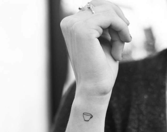 photo blanc et noir illustrant tatouage poignet femme à design minimaliste avec un petit dessin en encre à motif café