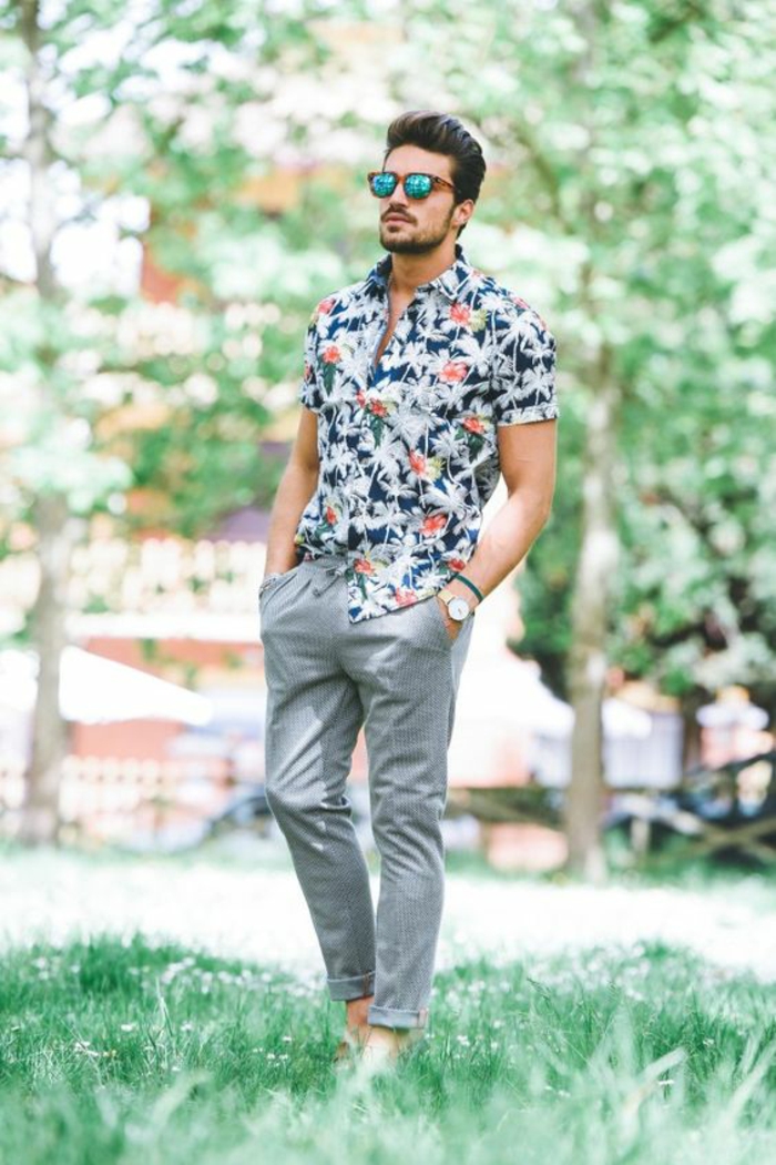 look d'été, vêtement homme classe, chemise manches courtes aux motifs fleuris, pantalon gris plus large dans la zone des poches, lunettes de soleil aux verres bleus 