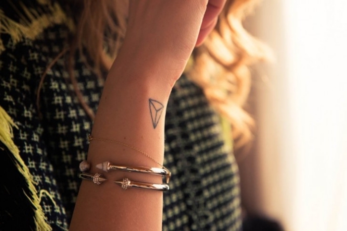 joli mini tattoo discret aux lignes simples et design géométrique réalisé sur le poignet d'une femme aux cheveux longs blonds 