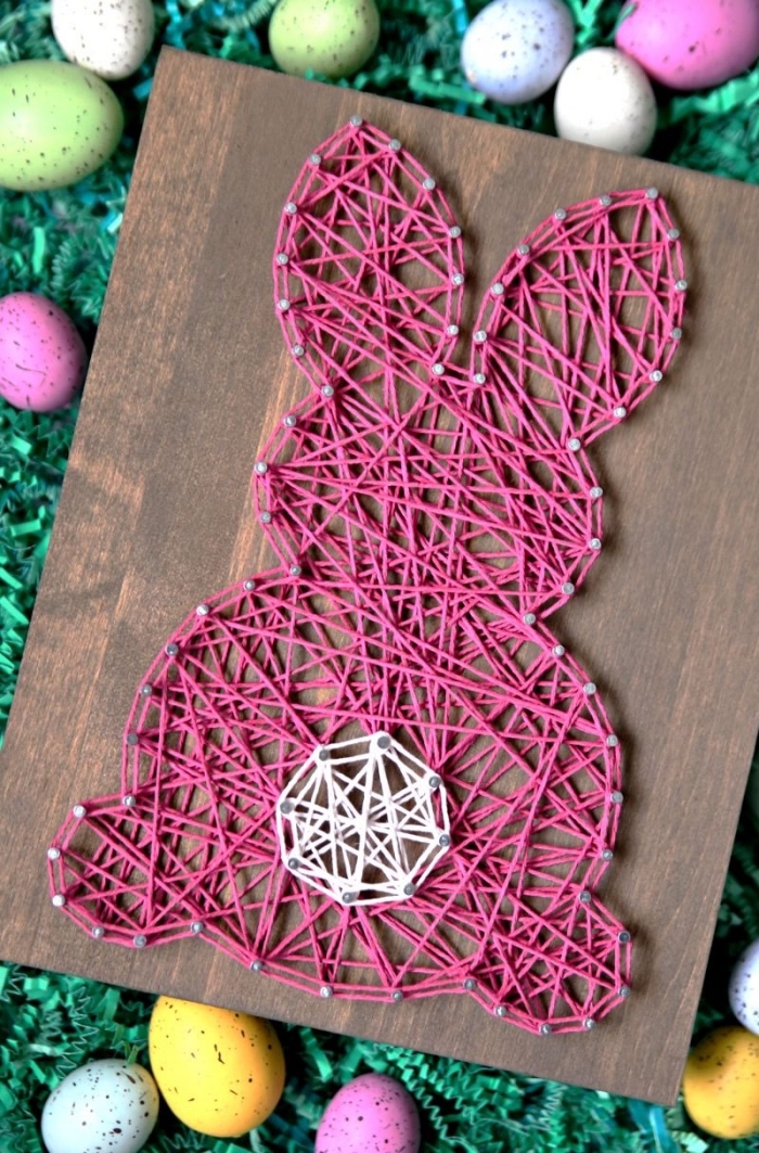 quelle déco de Pâques réaliser avec les enfants, modèle de tableau de bois foncé décoré de fil rose et blanc en forme de lapin