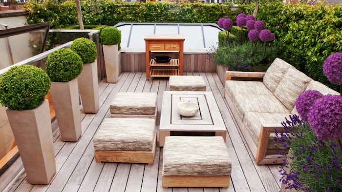 exemple d aménagement extérieur de terrasse en bois composite, canapé, tabourets, table bois et coussins d assise gris et beige, buis taillé, fleurs