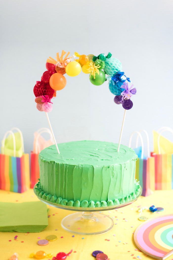 comment décorer un gateau arc-en-ciel, un cake au glaçage vert surmonté d'un cake topper personnalisé avec des boules en papier 