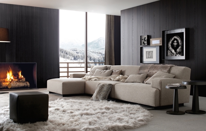 déco chaleureuse et comfortable dans un salon aux murs foncés avec cheminée et canapé d'angle beige, modèle de tapis en fausse fourrure blanche