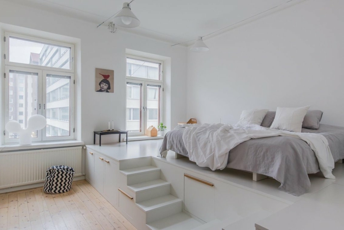 jolie chambre à coucher blanche et grise, escalier blanc et petite estrade pour le lit