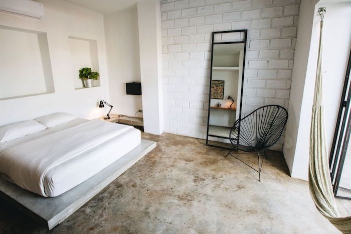 matelas blanc sur plate forme bois, sol effet béton, mur en briques blanches, chaise industrielle noire, niches murales