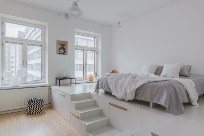 petit escalier blanc dans la chambre à coucher, lit gris et blanc, sol en planches, lampe design indistriel