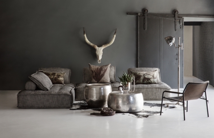 ambiance rustique dans un salon vaste aux murs gris foncé et plancher blanc avec canapé d'angle foncé et tapis imitation peau animale
