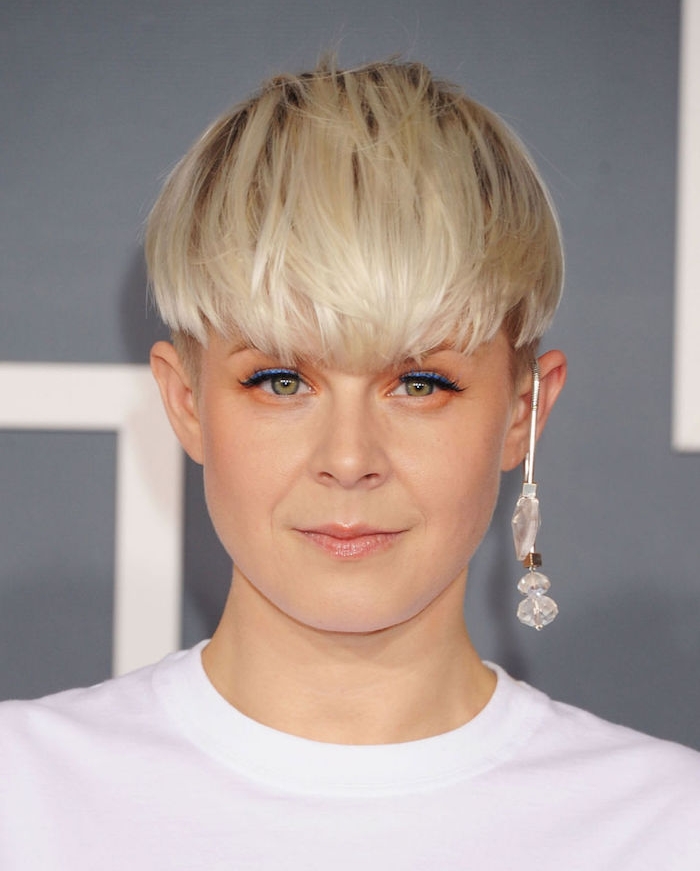 coupe femme courte cheveux coloration blond polaire cheveux ramenés en avant tombant sur le front, tee shirt blanc, boucle d oreille originale