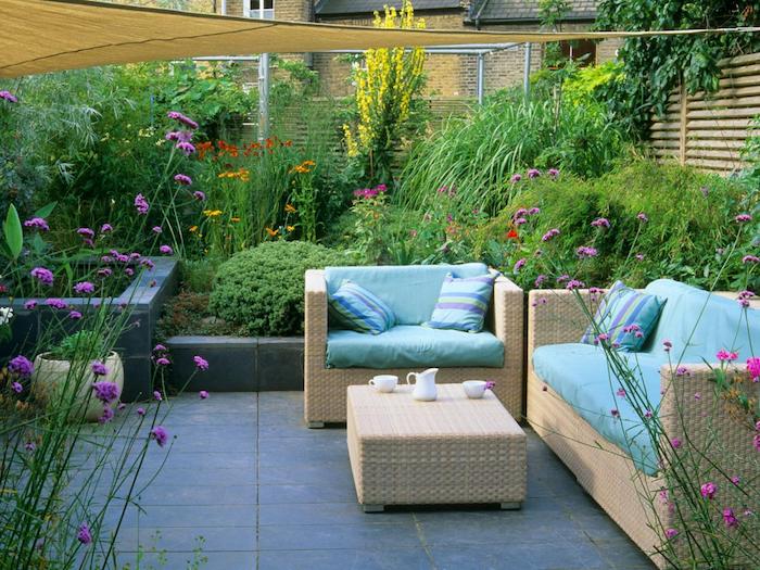 décoration terrasse revetement de dalles, canapé et fauteuil en rotin, table basse rotin, jardin à l anglaise avec arbustes, arbres et fleurs