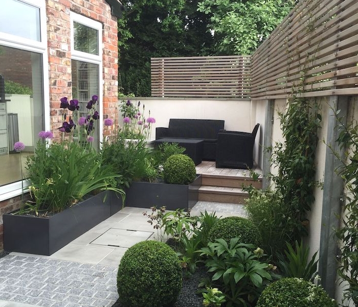 decoration jardin terrasse en bois avec salon de jardin en mobilier noir, bacs à fleurs noirs, buis taillés et autres fleurs